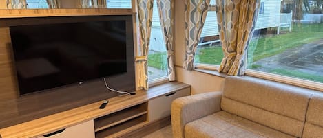 A compact living space with a flat-screen TV on a wooden stand, a sofa, and curtains on the windows.
