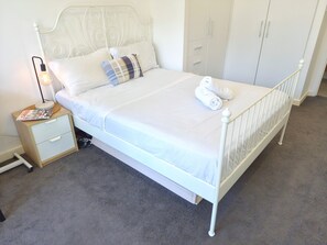 A white metal bed with a headboard, a bedside table with a lamp, and a wardrobe in a room with grey carpet. - Contemporary 2BDR APT with 2 Baths in Homebush (Homebush)
