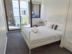 A bedroom with a white bed, a bedside table, a lamp, and a view of the outside. - Contemporary 2BDR APT with 2 Baths in Homebush (Homebush)
