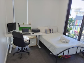 A bedroom with a bed, a desk with a laptop, a chair, and a window with a view of buildings. - Contemporary 2BDR APT with 2 Baths in Homebush (Homebush)