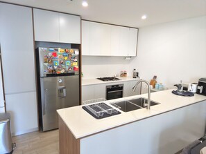 A modern kitchen with a stainless steel refrigerator, a built-in dishwasher, a sink with a faucet, and a countertop with a kettle and toaster. - Contemporary 2BDR APT with 2 Baths in Homebush (Homebush)
