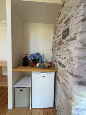A compact kitchenette with a white refrigerator, a wooden countertop, and a stone wall.
