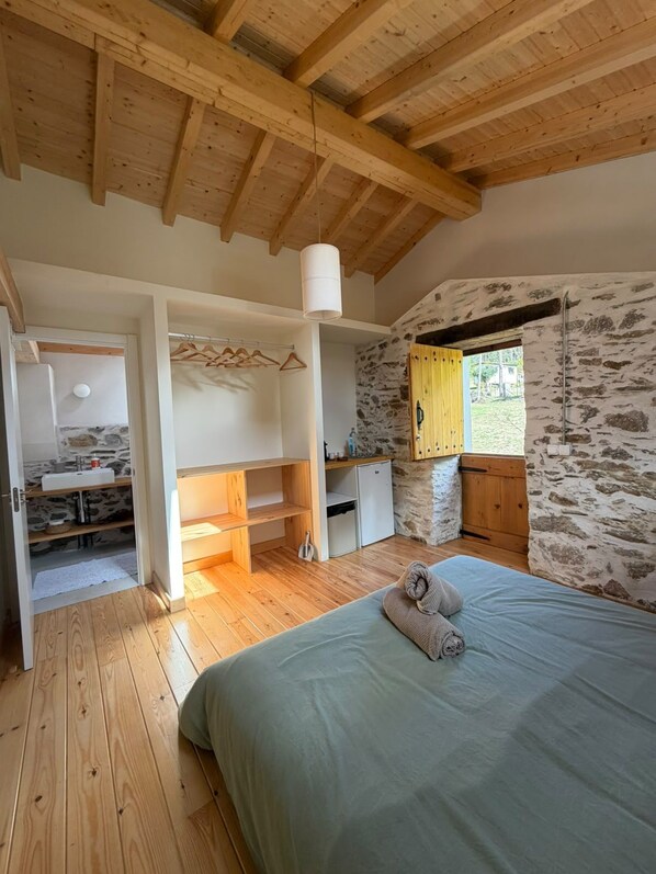 Une chambre avec un lit, des poutres en bois, un mur en pierre, une petite kitchenette et une salle de bain avec un lavabo.