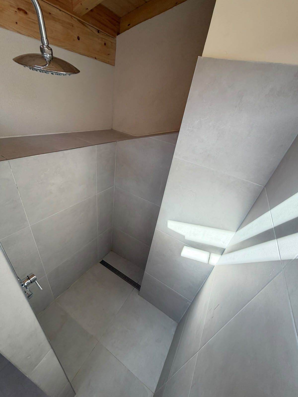 A shower with a modern design, featuring a curved showerhead and a corner tile layout.