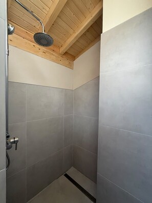 A shower with a handheld showerhead, tiled walls, and a wooden ceiling.