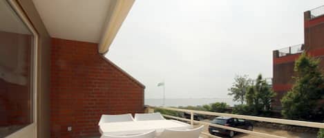 Uma varanda com mesa e cadeiras, vista para o mar e um muro de tijolos.