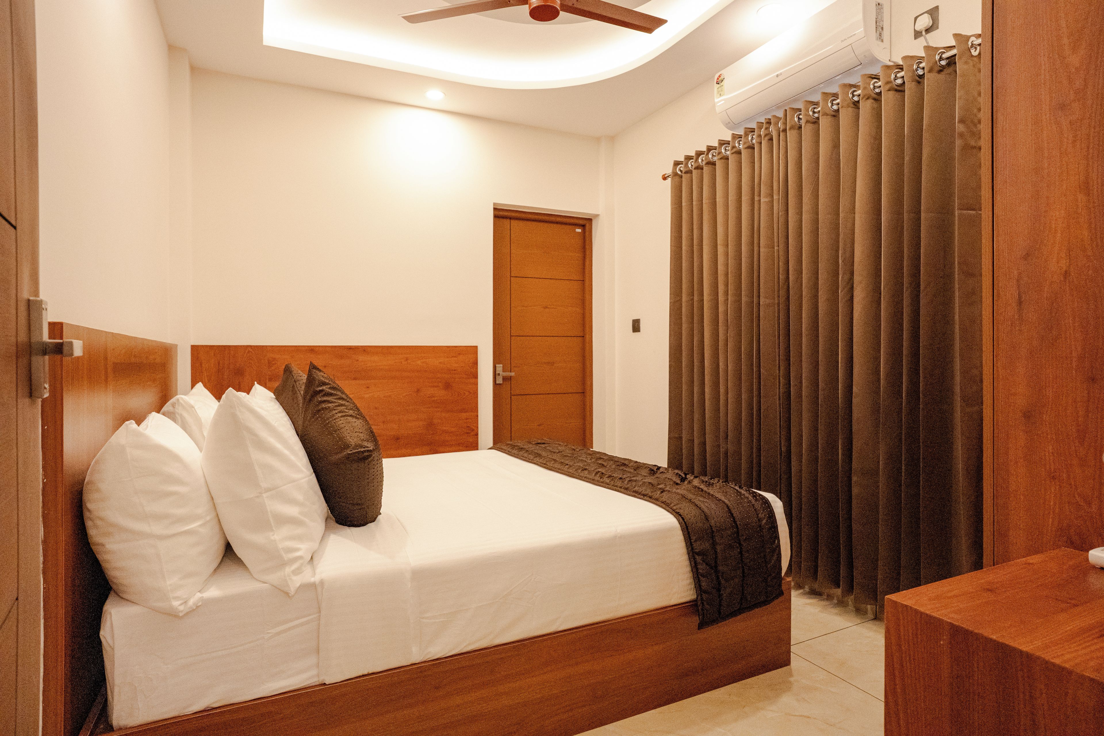 Un dormitorio con cama, cabecera de madera, mesita de noche, puerta y cortina.