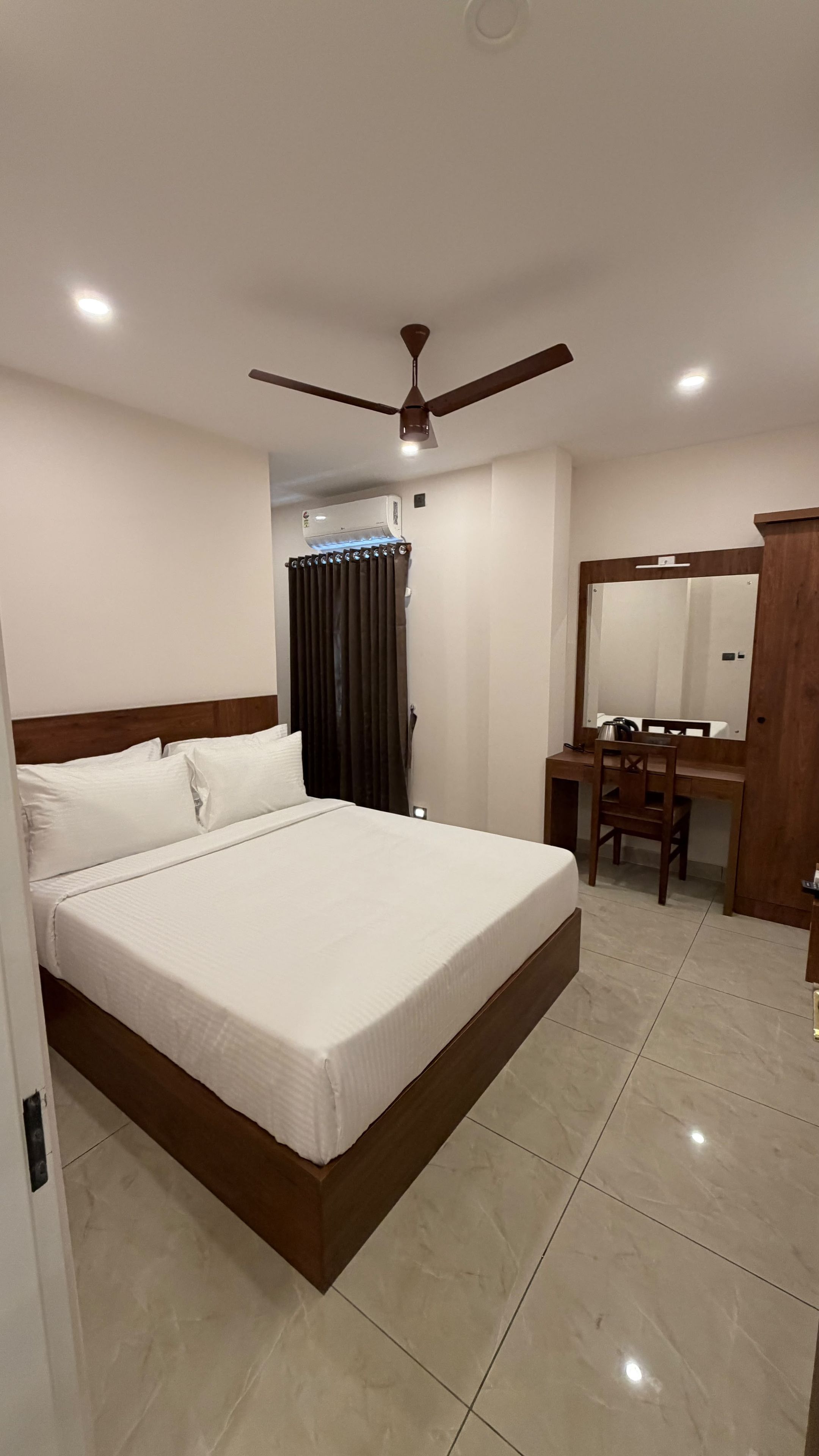 Una habitación de hotel con cama, escritorio, silla, ventilador de techo y aire acondicionado.
