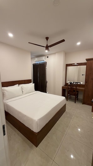 A hotel room with a bed, a desk, a chair, a ceiling fan, and an air conditioning unit. - HAVENS BAY (Kumily)