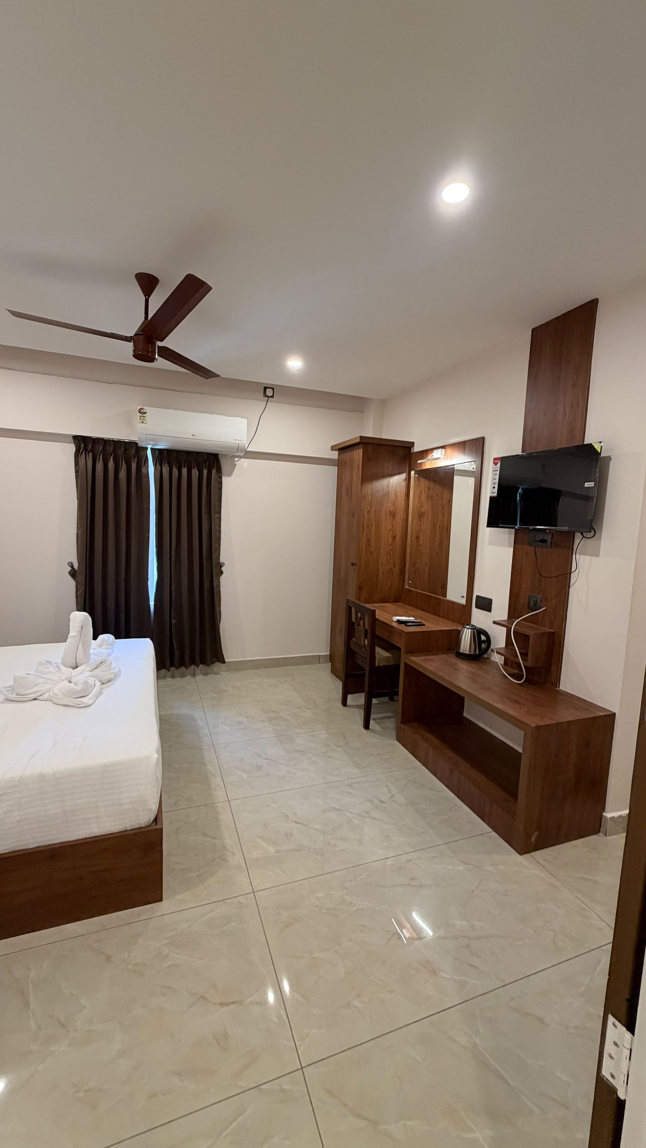 Una habitación de hotel con cama, escritorio, televisión y ventilador de techo.