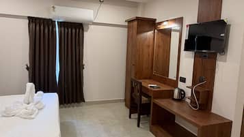 Una habitación de hotel con cama, escritorio, televisión y ventilador de techo.