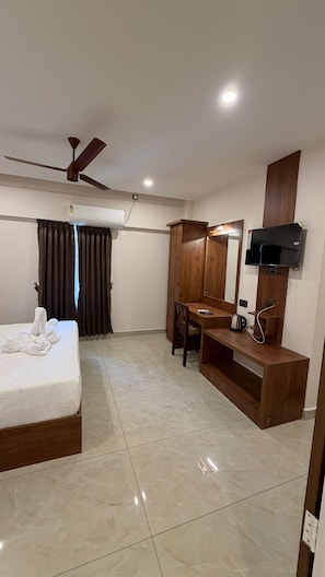 A hotel room with a bed, a desk, a television, and a ceiling fan. - HAVENS BAY (Kumily)