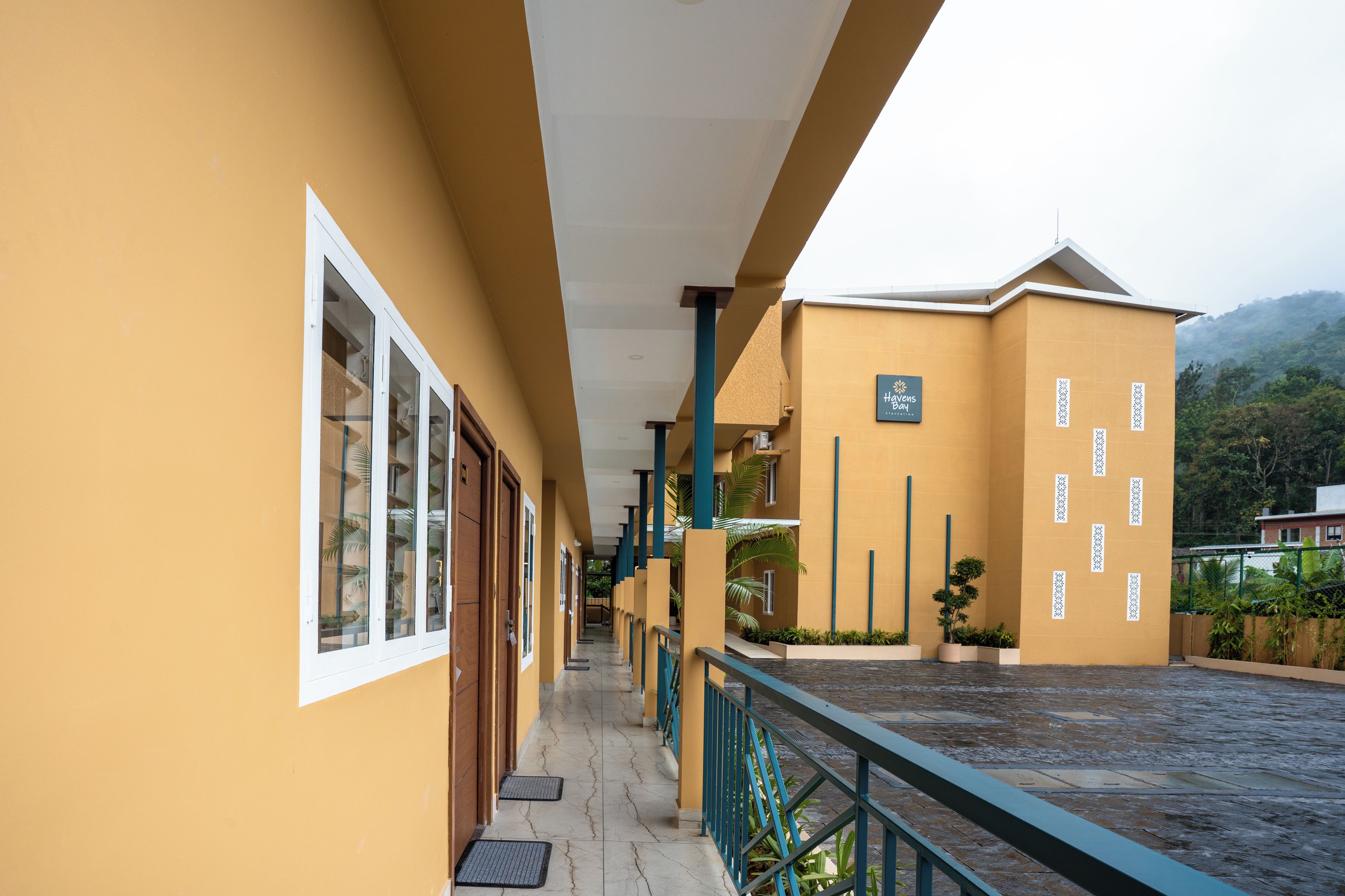 A hotel corridor with a yellow exterior, a covered walkway, and a view of a mountainous landscape.