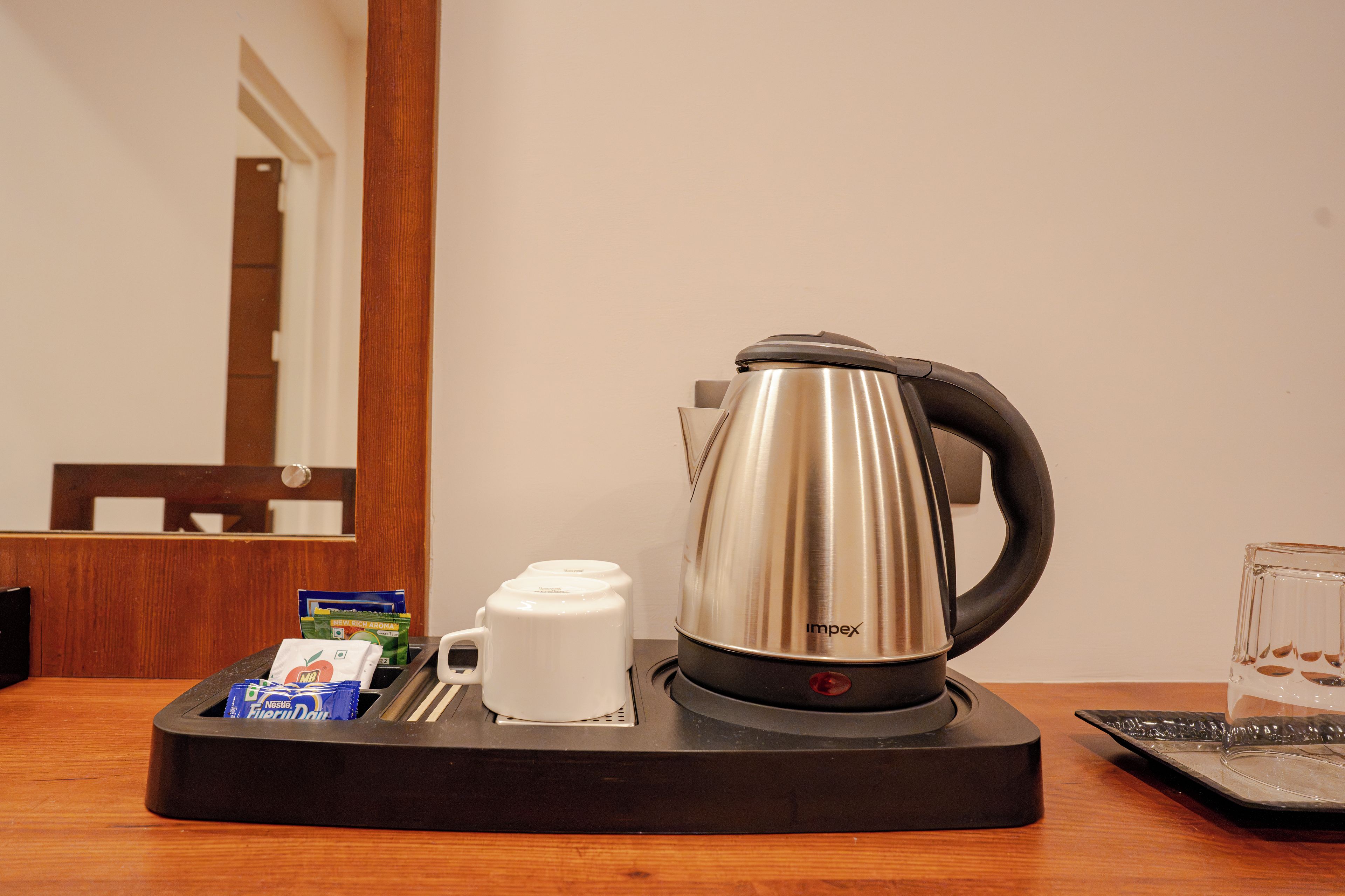 A coffee maker with a tray, a glass, and some coffee pods on a wooden table.
