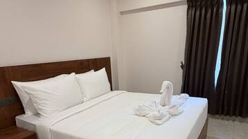 Una cama bien hecha con cabecera de madera, una mesita de noche pequeña y un ventilador de techo.