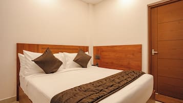 A neatly made bed with white linens and two brown pillows, a wooden headboard, and a wooden wardrobe in a room with white walls.