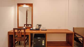 A hotel room with a wooden desk, a chair, a mirror, a refrigerator, and a coffee maker.