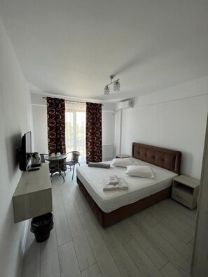 Habitació d'hotel amb llit, escriptori, cadira, televisió i finestra amb cortines.