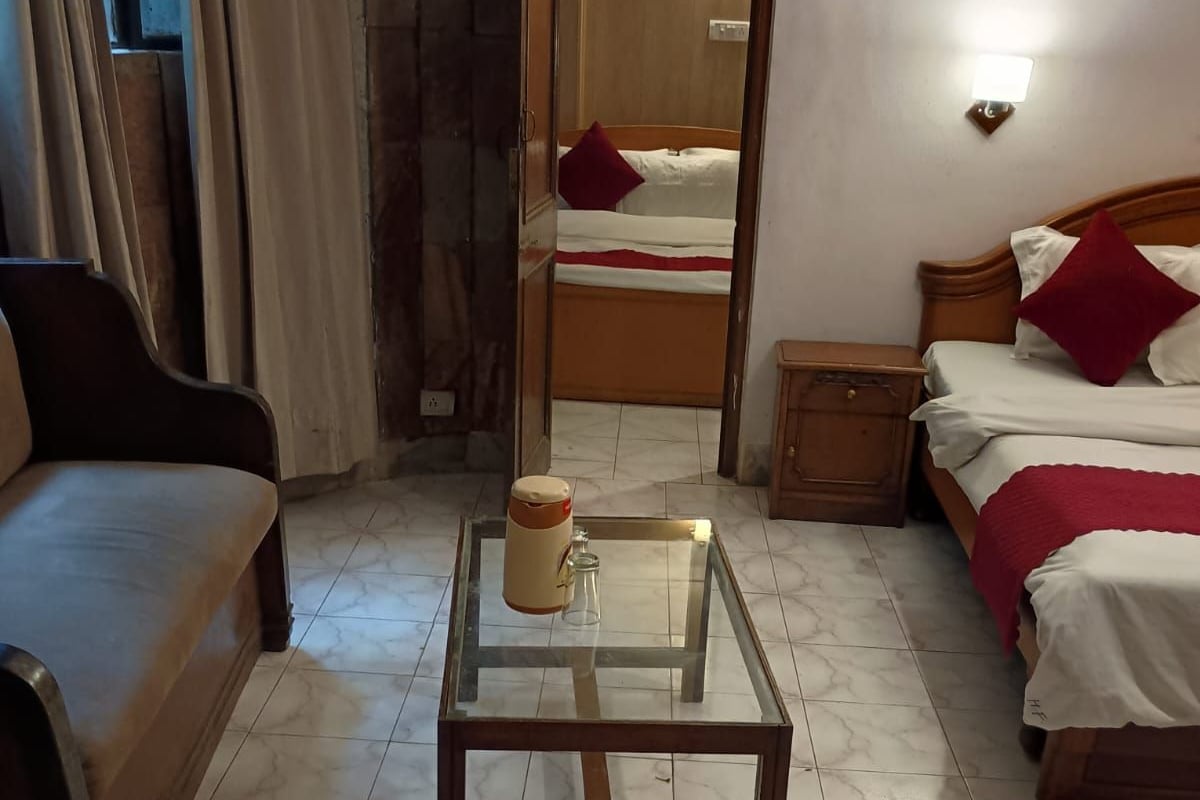A hotel room with a bed, a sofa, a glass-top table with a mug, and a nightstand.