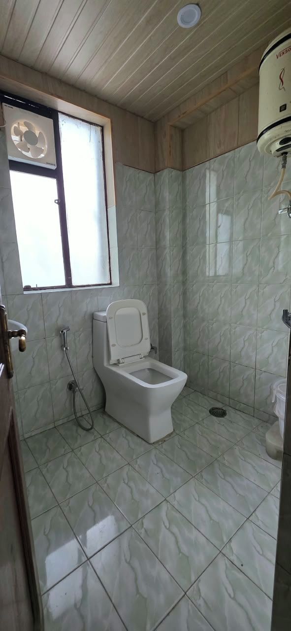 A small bathroom with a toilet, a window, and a shower.