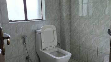 A small bathroom with a toilet, a window, and a shower.