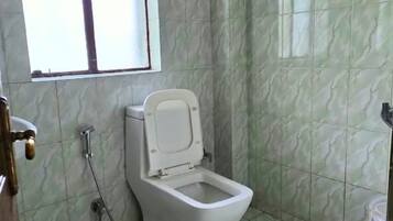 A bathroom with a toilet, shower, and a window.