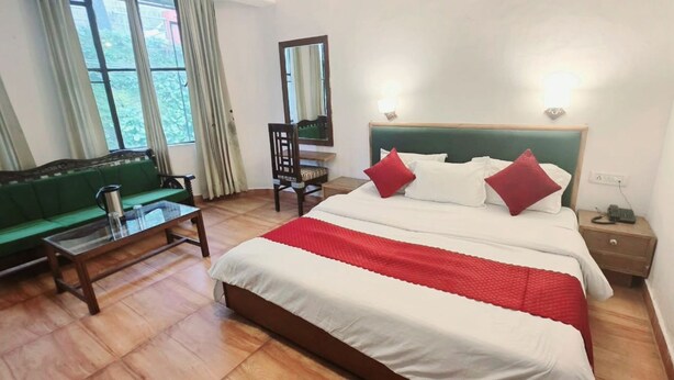 A hotel room with a bed, a green sofa, a wooden coffee table, a chair, a bedside table with a lamp, and a window with curtains. - HOTEL FILIGREE THE MALL MUSSOORIE (Mussoorie)