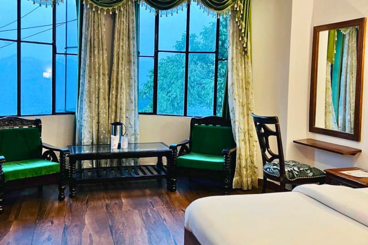 Quarto de hotel com uma cama grande, uma mesa com cadeiras e vista pela janela.