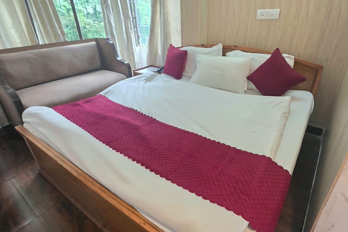 A bed with a white and red bedspread, a wooden headboard, and a brown sofa.