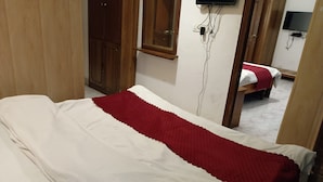 A single bed with a white and red bedspread, a wooden wardrobe, a television mounted on the wall, and a wooden door. - HOTEL FILIGREE THE MALL MUSSOORIE (Mussoorie)