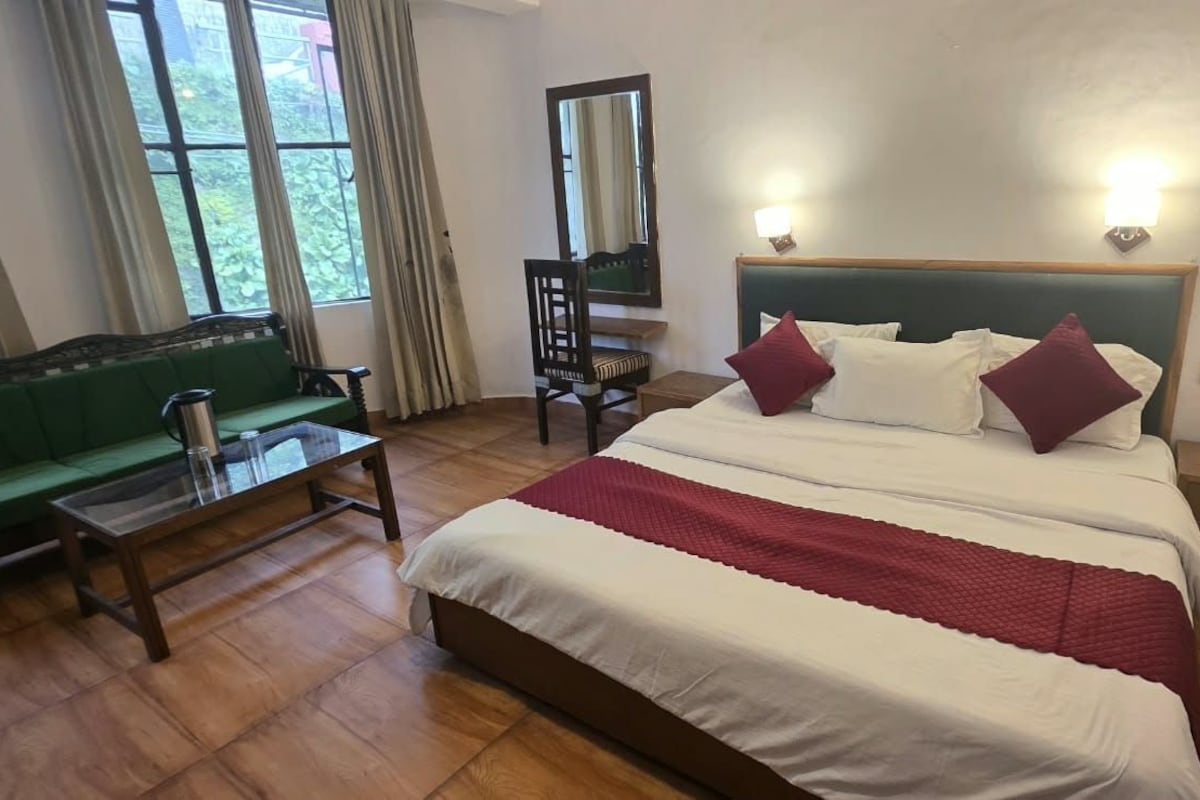 A hotel room with a bed, a green sofa, a wooden table, a chair, and a mirror.