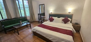 Hotellihuone, jossa on sänky, vihreä sohva, puinen pöytä, tuoli ja peili.