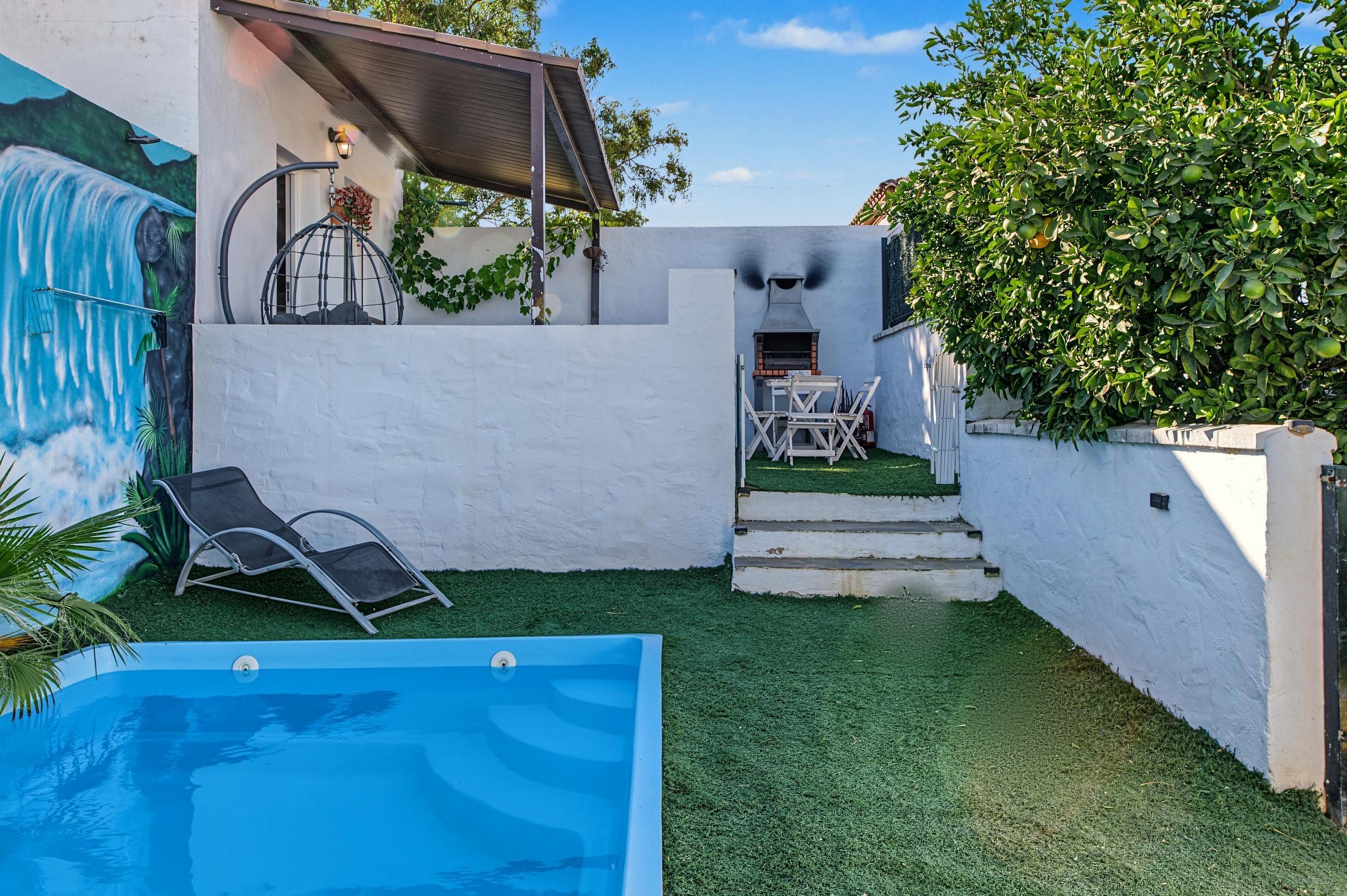 Un patio trasero con piscina, una zona de estar cubierta y una parrilla.