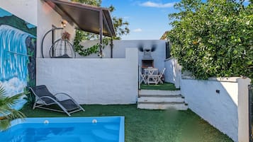 Un patio trasero con piscina, una zona de estar cubierta y una parrilla.