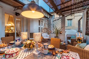An outdoor dining area with wicker furniture, a table set with plates and glasses, and a hanging light fixture. - Modern Apartment With Terrace, Lucca (Lucca)