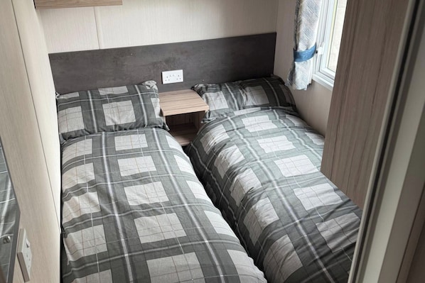 A compact bedroom with two beds, a small bedside table, and a window with curtains.