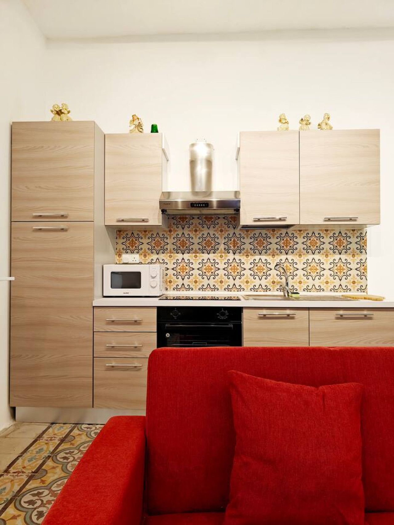 Een keuken met houten kastjes, een magnetron, een fornuis en een rode bank op de voorgrond.
