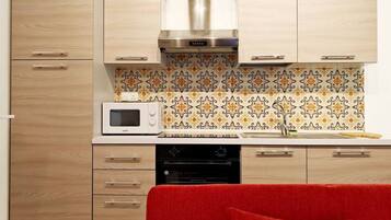 Een keuken met houten kastjes, een magnetron, een fornuis en een rode bank op de voorgrond.