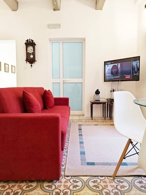 Een woonkamer met een rode bank, een televisie, een klok en een kamerkleed met een patroon.