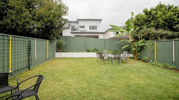 Ein Garten mit Rasenfläche, einem Tisch mit Stühlen und einem grünen Zaun.