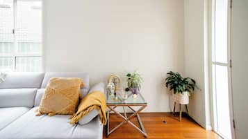 Ein Wohnzimmer mit einer Couch, einem Glastisch und zwei Zimmerpflanzen.