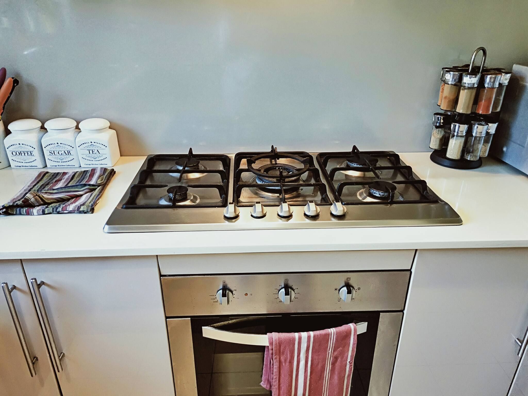 Una cucina con un piano cottura a gas, un set di barattoli etichettati caffè, zucchero e tè, e una spechiera.