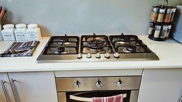 Una cucina con un piano cottura a gas, un set di barattoli etichettati caffè, zucchero e tè, e una spechiera.