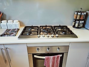 A kitchen with a gas stove, a set of jars labeled coffee, sugar, and tea, and a spice rack.