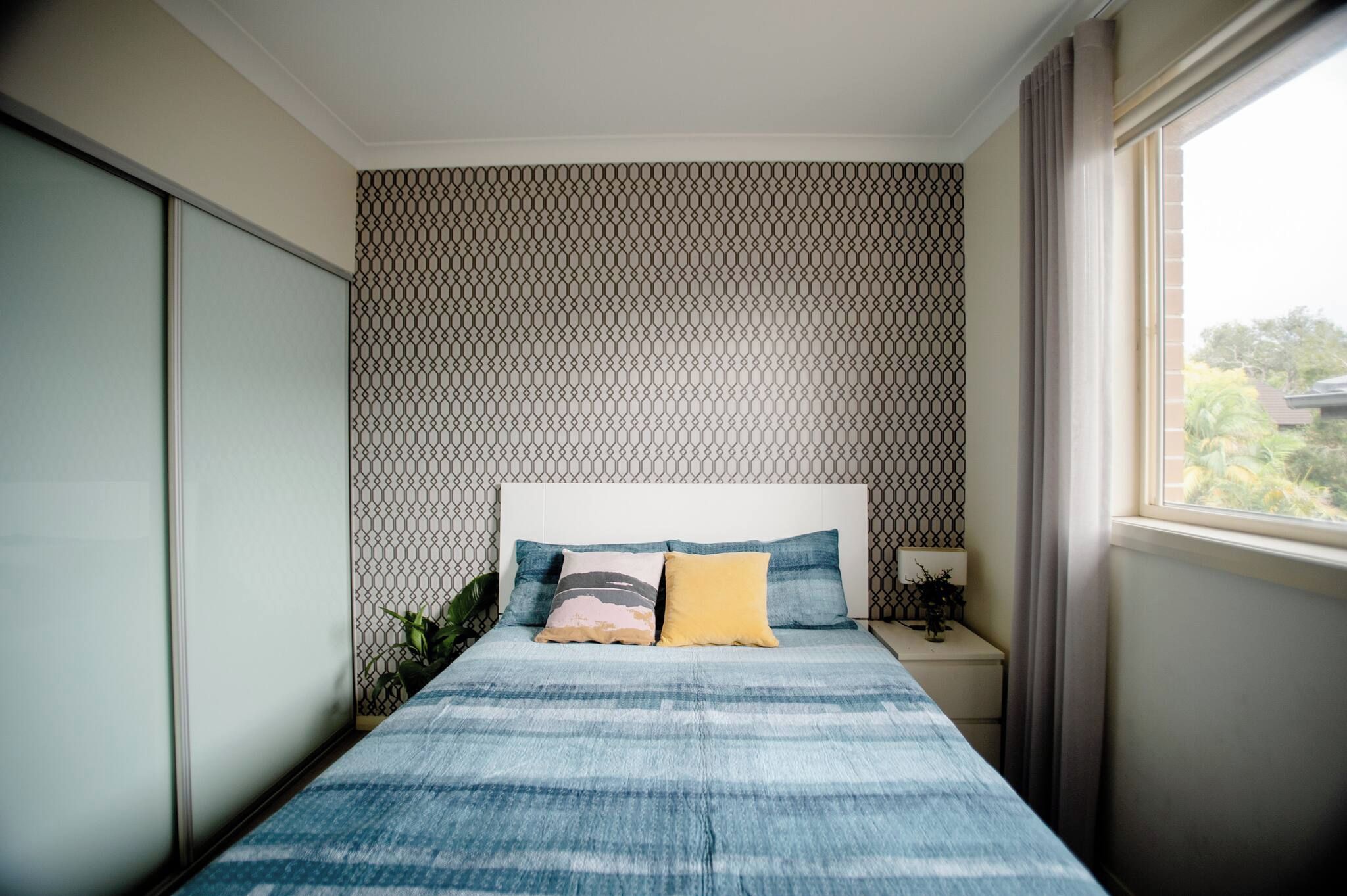 A bedroom with a bed, a nightstand, a lamp, and a window.