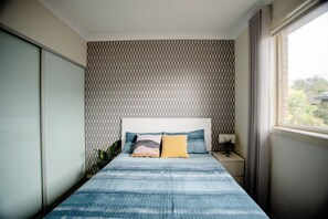A bedroom with a bed, a nightstand, a lamp, and a window.