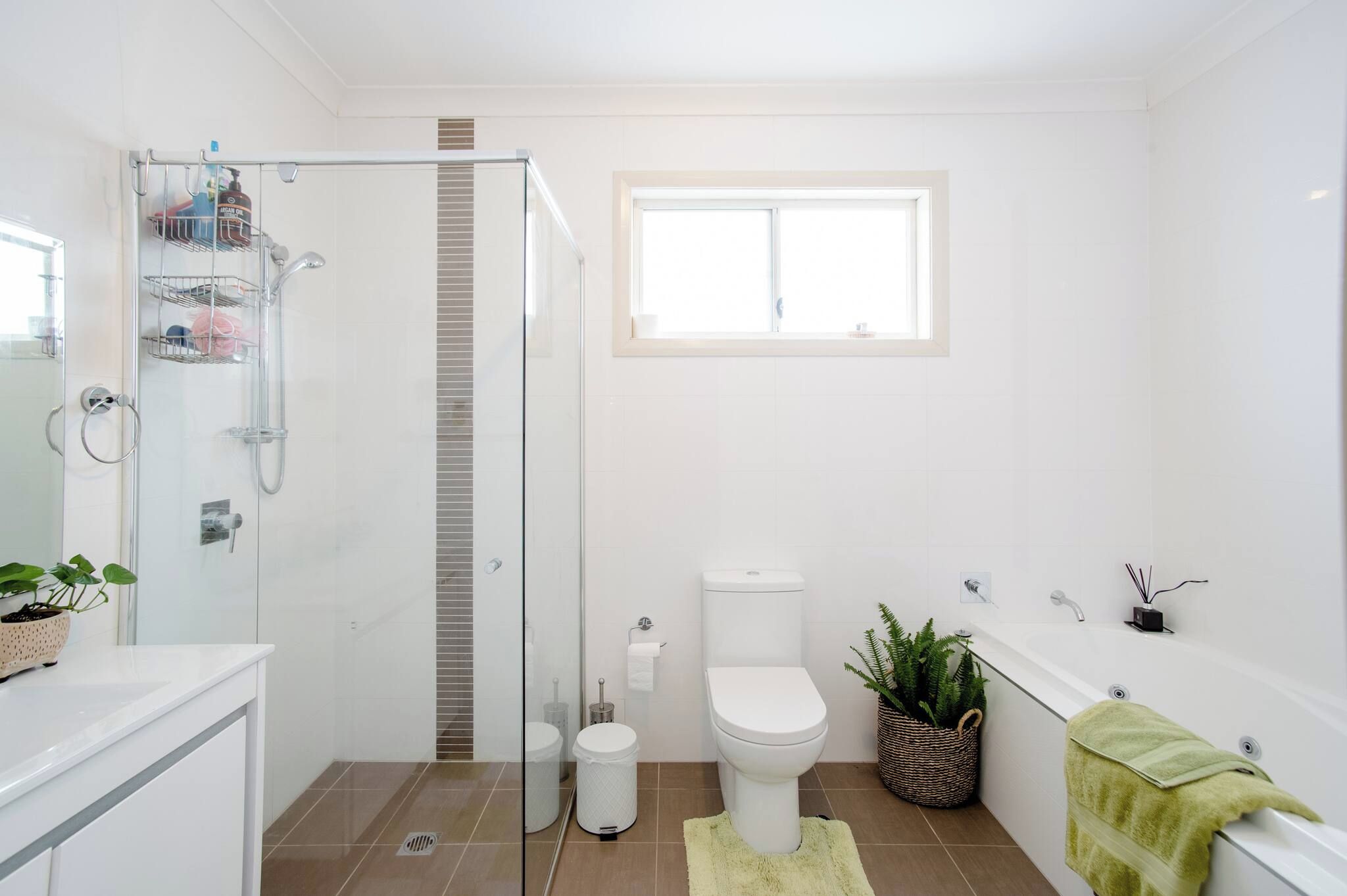 A modern bathroom with a glass shower enclosure, a toilet, a bathtub, and a window providing natural light.