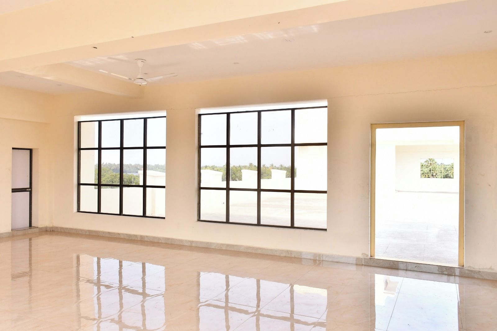 A spacious room with large windows, a ceiling fan, and a reflective floor.