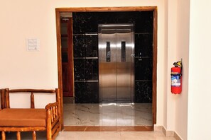 An elevator with a metallic finish, a fire extinguisher mounted on the wall, and a wooden bench in the foreground. - Grami Cafe (Puducherry)
