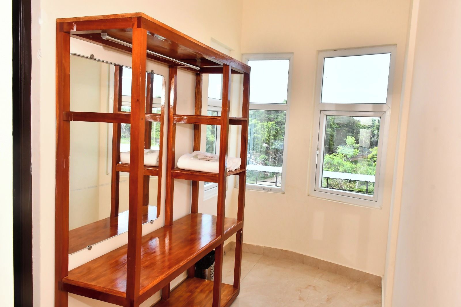 Una habitación con un armario de madera, dos ventanas con vistas a zonas verdes y suelo de baldosas.